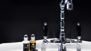 Un lavamanos con grifo cromado, dos frascos de perfume y un espejo con marco decorativo.