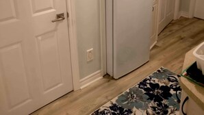 Una cucina compatta con mobili bianchi, frigorifero integrato e pavimento in legno.