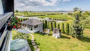 Un jardin avec un jacuzzi, un espace salon et une vue sur une rivière où naviguent des bateaux.