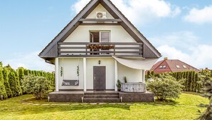Une maison à deux étages, avec un toit sombre, des murs blancs et un porche à l’avant où se trouve une balançoire.