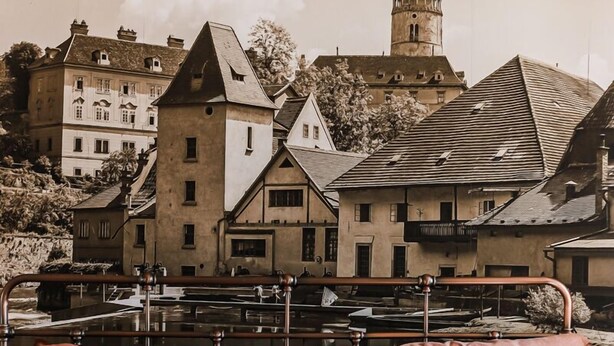 A bed with metal headboard and pillows, a view of buildings and a tower in the background. - Velký stylový byt v centru Krumlova (Cesky Krumlov)