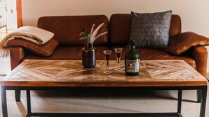 A wooden coffee table with a bottle and glasses, a vase with dried plants, and a metal container on a brown leather sofa. - Velký stylový byt v centru Krumlova (Cesky Krumlov)