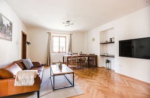 A living room with a sofa, coffee table, dining table, chairs, a TV, and a window with curtains. - Velký stylový byt v centru Krumlova (Cesky Krumlov)