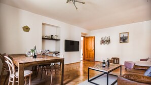 A modern living room with a wooden dining table, leather sofa, and a flat-screen TV mounted on the wall. - Velký stylový byt v centru Krumlova (Cesky Krumlov)