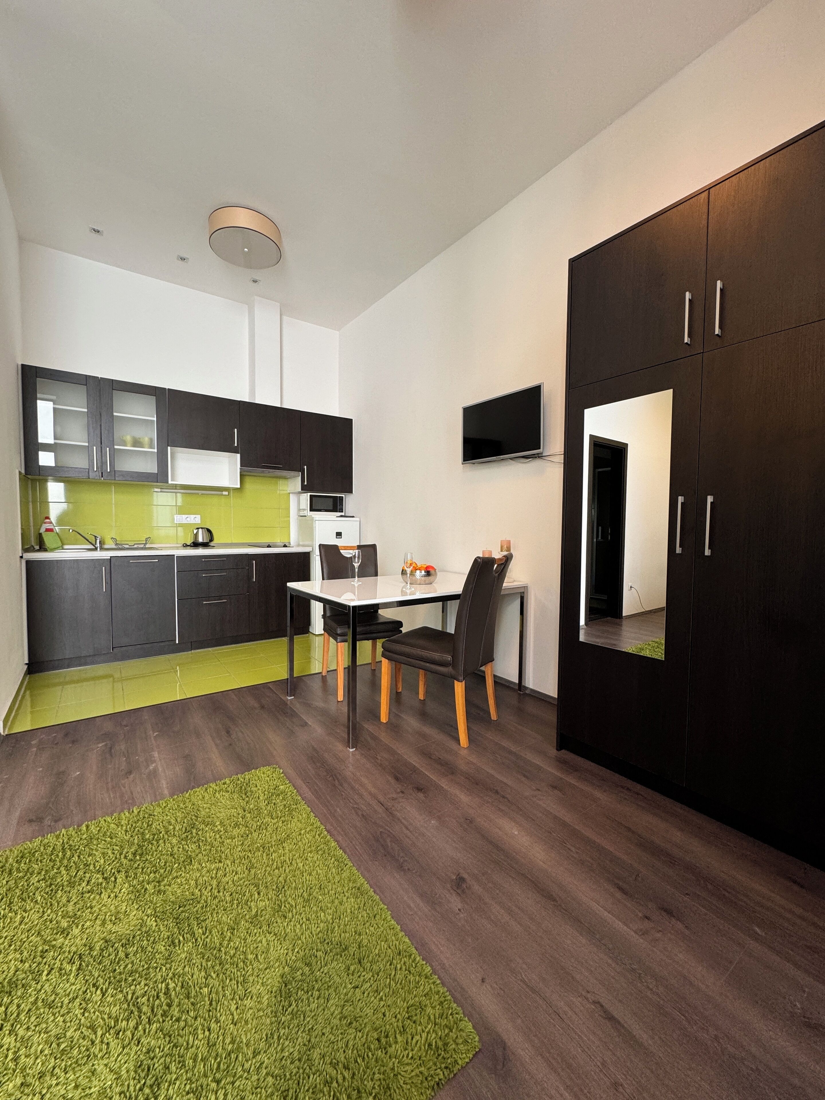 Una cocina moderna con gabinetes oscuros, un protector de salpicadero verde y una zona de comedor con mesa y sillas.
