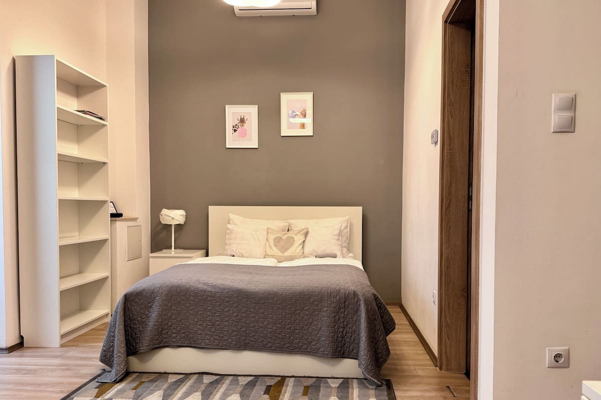 Un dormitorio con cama, mesita de noche, aire acondicionado de pared y una puerta.