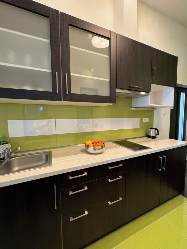 A modern kitchen with dark cabinets, a stainless steel sink, and a countertop with a bowl of fruit.