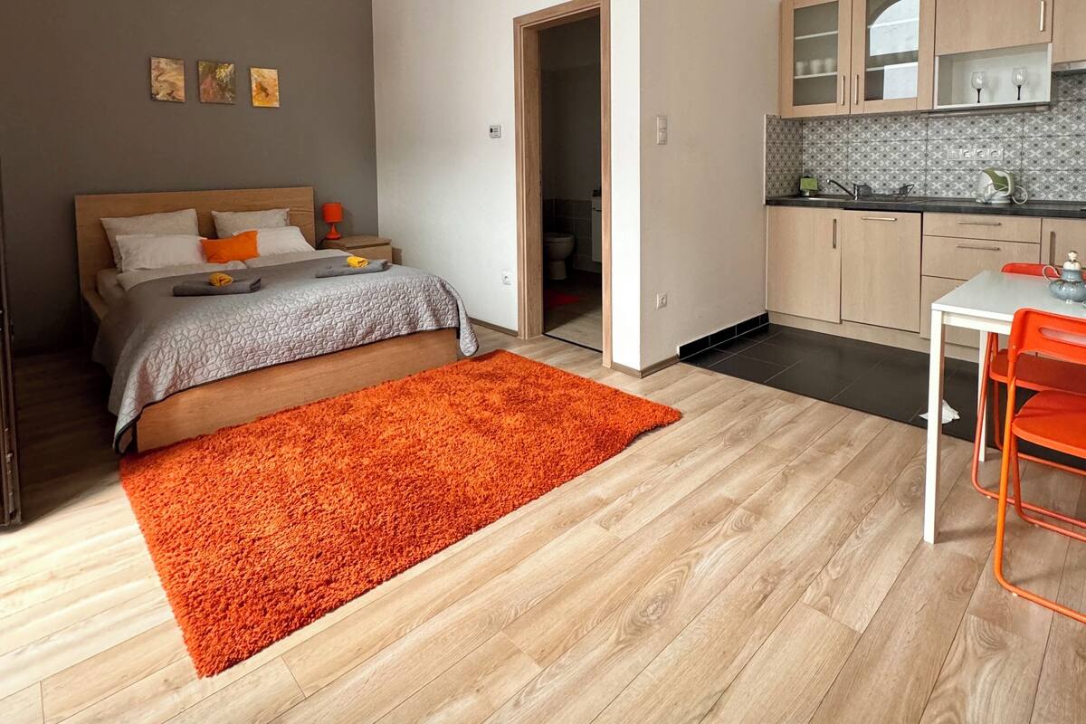 Un dormitorio moderno con una cama grande, un tapete naranja brillante y una pequeña cocina con una mesa y sillas.