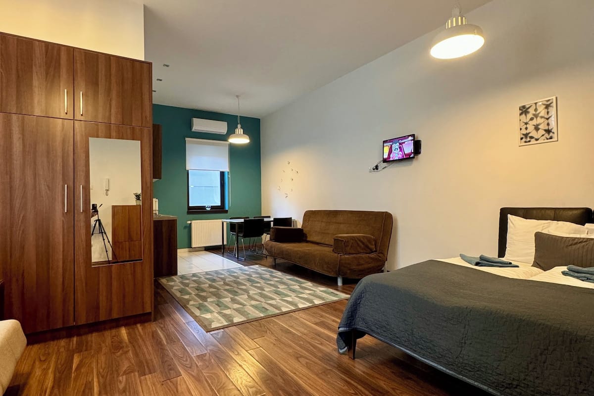 Un dormitorio moderno con un armario de madera, una cama con manta oscura, un sofá marrón y un televisor en la pared.