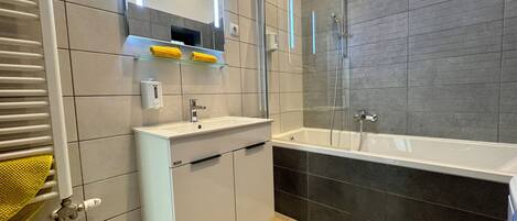 Un baño moderno con tocador blanco, cabina de ducha de cristal y bañera.