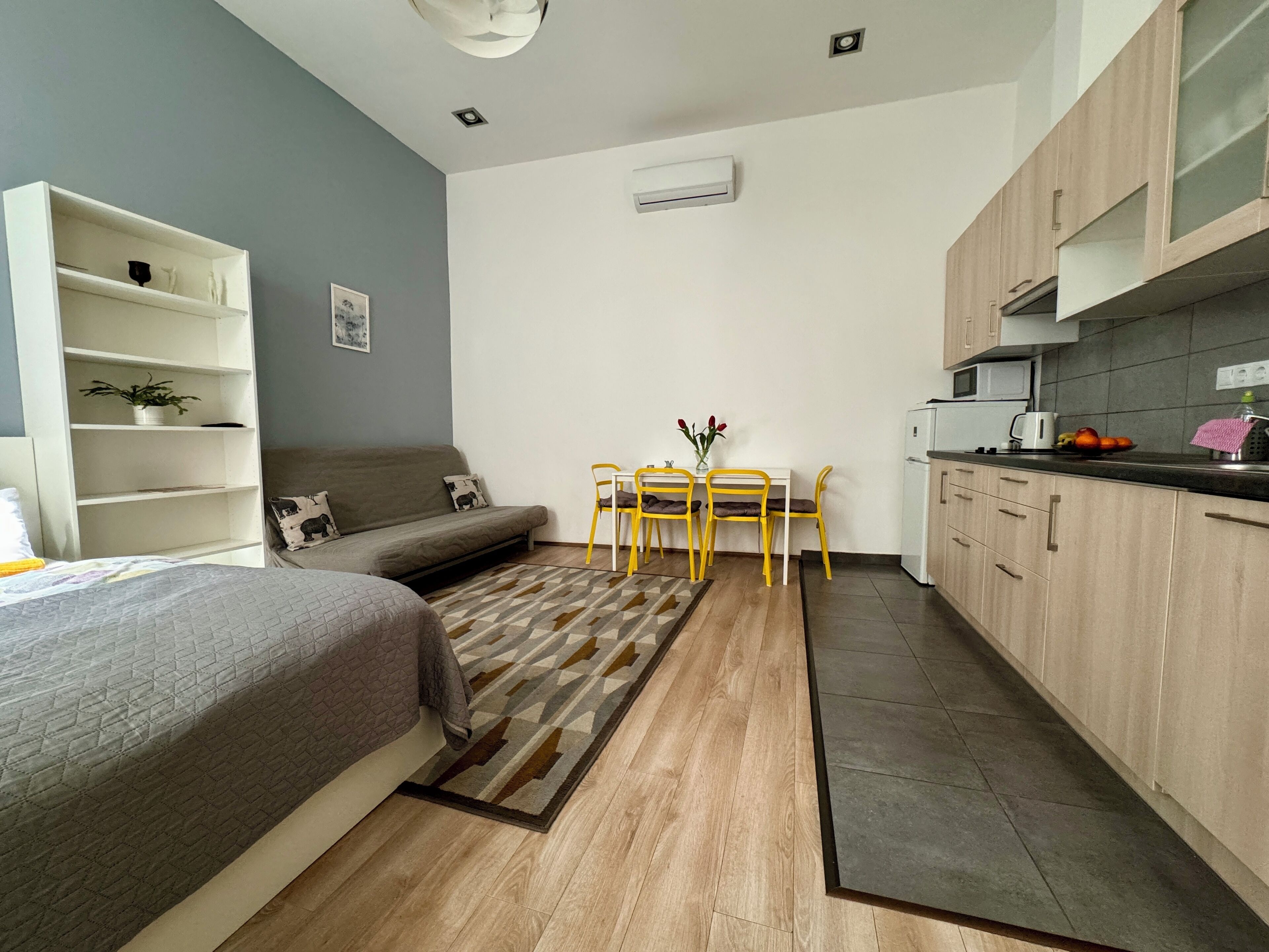 A compact living space with a bed, a sofa, a dining table with chairs, a kitchen area, and a built-in wardrobe.