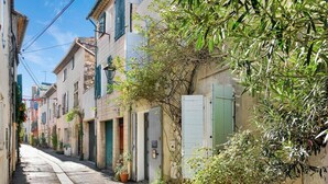 Une rue étroite bordée de bâtiments traditionnels, dont certains sont dotés de volets et de plantes en pot.