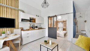 Une cuisine moderne avec des meubles blancs, un coin repas avec une table dressée pour deux personnes, et un salon avec un canapé et une petite table.