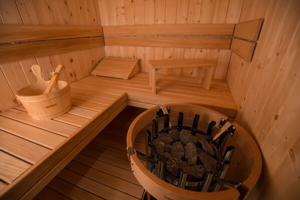 Eine Holzsauna mit Bänken, einem Holzeimer und einem steinbelegten Becken.