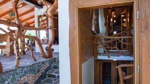 Una escalera de madera junto a un muro de piedra, una puerta de madera y un techo con vigas de madera.