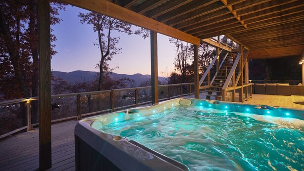 Una vasca idromassaggio su un pontile in legno con vista sulle montagne.