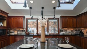 Una cucina moderna con mobili in legno, un'isola centrale con due piatti e bicchieri, un vaso con fiori secchi e un lucernario.