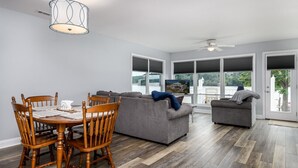 A modern living room with a dining table, wooden chairs, a grey sofa, and a ceiling fan. - Lakefront, two bedroom, full bath. Relax, swim, kayak & fish on Lake Lookout. (Claremont)