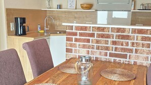 Una mesa de comedor con individuales tejidos, una jarra de vidrio y una cocina moderna con salpicadero de ladrillo y vigas de madera en el techo.
