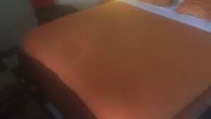 A bed with an orange bedspread, a nightstand with a lamp, and a red chair. - Motel Jupiter (Sangmélima)