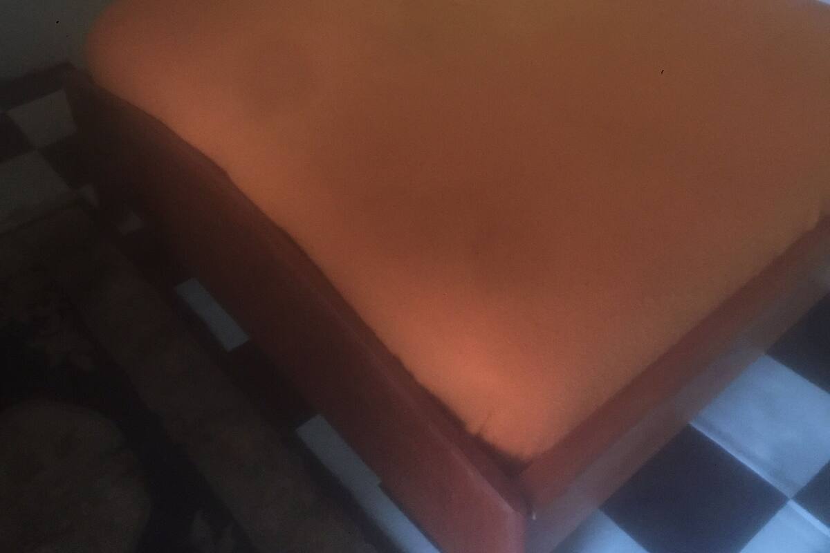 Una cama con una colcha naranja, una mesita de noche con una lámpara y una silla roja.