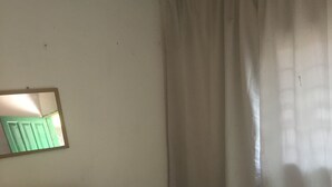 A bedroom with a bed, a headboard, a mirror, and a window with curtains. - Motel Jupiter (Sangmélima)
