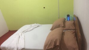 A single bed with a white sheet and two brown pillows, a bedside table with a lamp, and a green wall. - Motel Jupiter (Sangmélima)