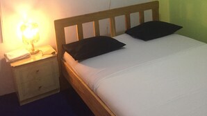 A single bed with a wooden headboard, two black pillows, and a bedside table with a lamp. - Motel Jupiter (Sangmélima)