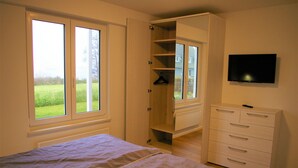 A bedroom with a bed, a wardrobe, a television, and a window with a view of a green landscape.