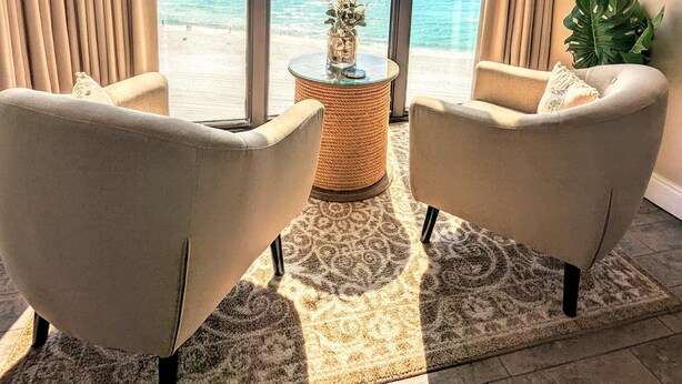 A room with two armchairs facing a large window with a view of the beach. - Exquisite Deluxe Vacation 7th floor Tower II (Panama City Beach)