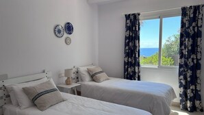 Un dormitorio con dos camas, una mesita de noche, una lámpara y vista al mar.