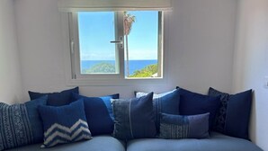 Una habitación con sofá, ventana con vista al mar y una puerta.