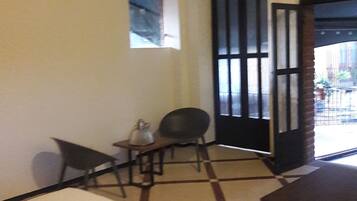 A hotel room with a bed, a small table with a chair, and a view through an open door.