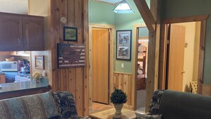 A cozy living room with a wooden bench, a small table with a plant, and a kitchen area visible in the background. - Tranquil Trailside (Custer)