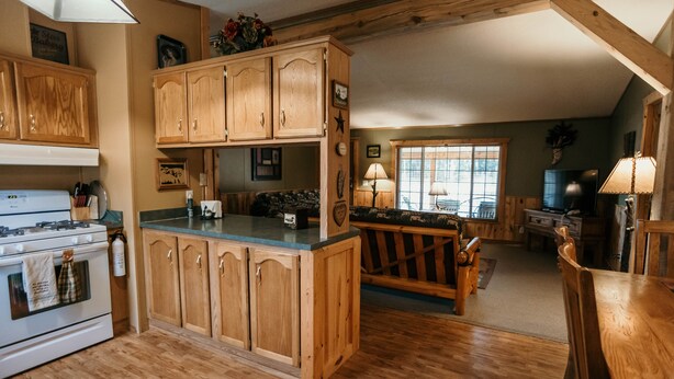 A kitchen with wooden cabinets, a stove, and a dining area with a wooden table and chairs. - Tranquil Trailside (Custer)