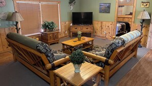 A cozy living room with a wooden sofa, a coffee table, and a television. - Tranquil Trailside (Custer)