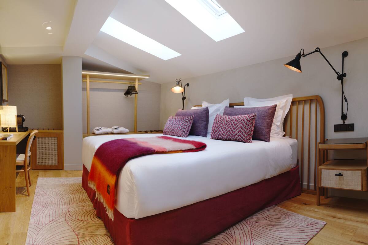 Une chambre à coucher moderne avec un grand lit, des fenêtres de toit, un bureau et une table de chevet.