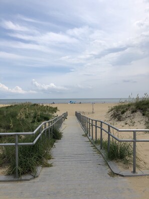 A concrete pathway leading to a beach with a railing on one side and grass on the other.