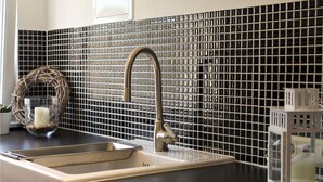 Et køkken med en stålvask, en moderne vandhane og en backsplash beklædt med små, firkantede fliser.