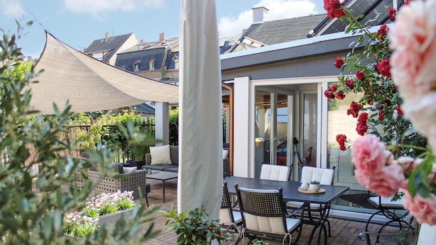 En terrasse med et bord og stole, omgivet af krukker med planter og blomster.