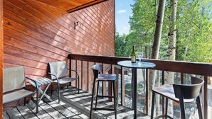 Een houten terras met buitenmeubels en een tafel, met uitzicht op een bebost gebied.