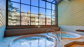 Een wellnessruimte met twee bubbelbaden en een groot raam met uitzicht op een gebouw.