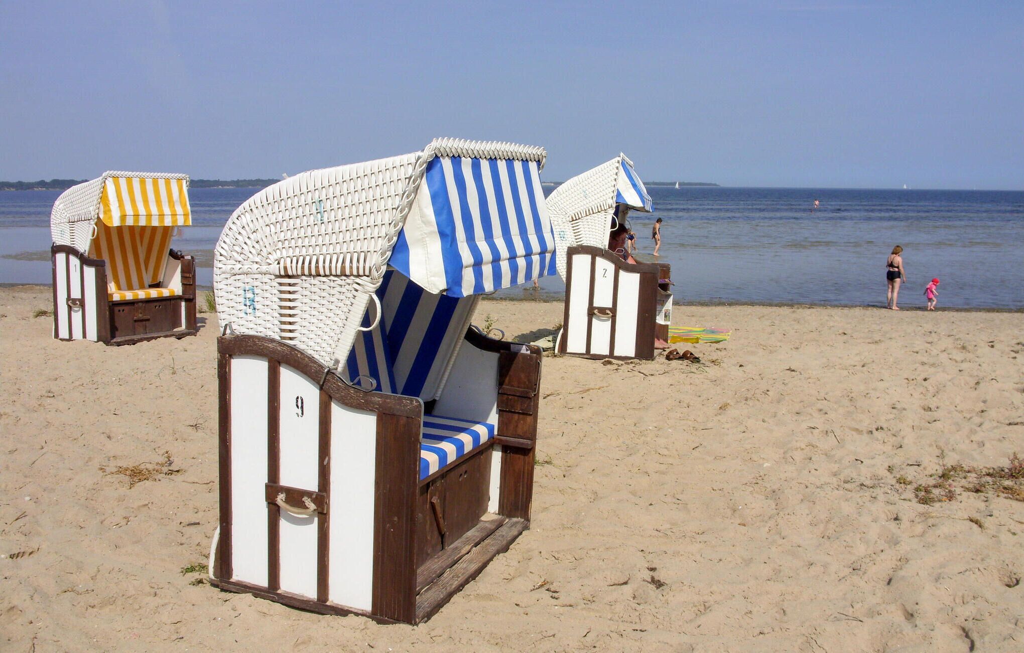Beach chairs with striped canopies and wooden frames, arranged on a sandy beach with the sea in the background.
