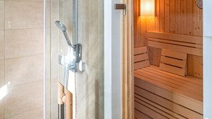 Een douchecabine met glazen wanden, een douchekop die je in de hand kunt houden, een houten sauna bank en een wandradiator.