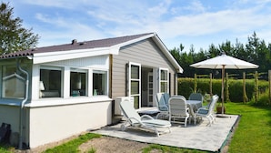 Una casa con un patio cubierto que cuenta con mobiliario exterior y un paraguas grande.