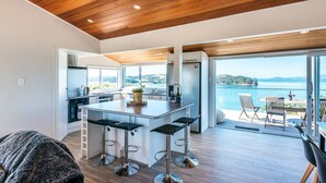 A modern kitchen with a central island, bar stools, and a view of a lake. - Ocean View (Waiheke Island)
