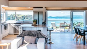 A modern kitchen with a large island, a dining area with a view, and a cozy seating area. - Ocean View (Waiheke Island)