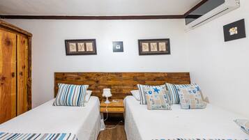 A room with two beds, wooden headboard, white walls, framed pictures, and a wooden wardrobe.
