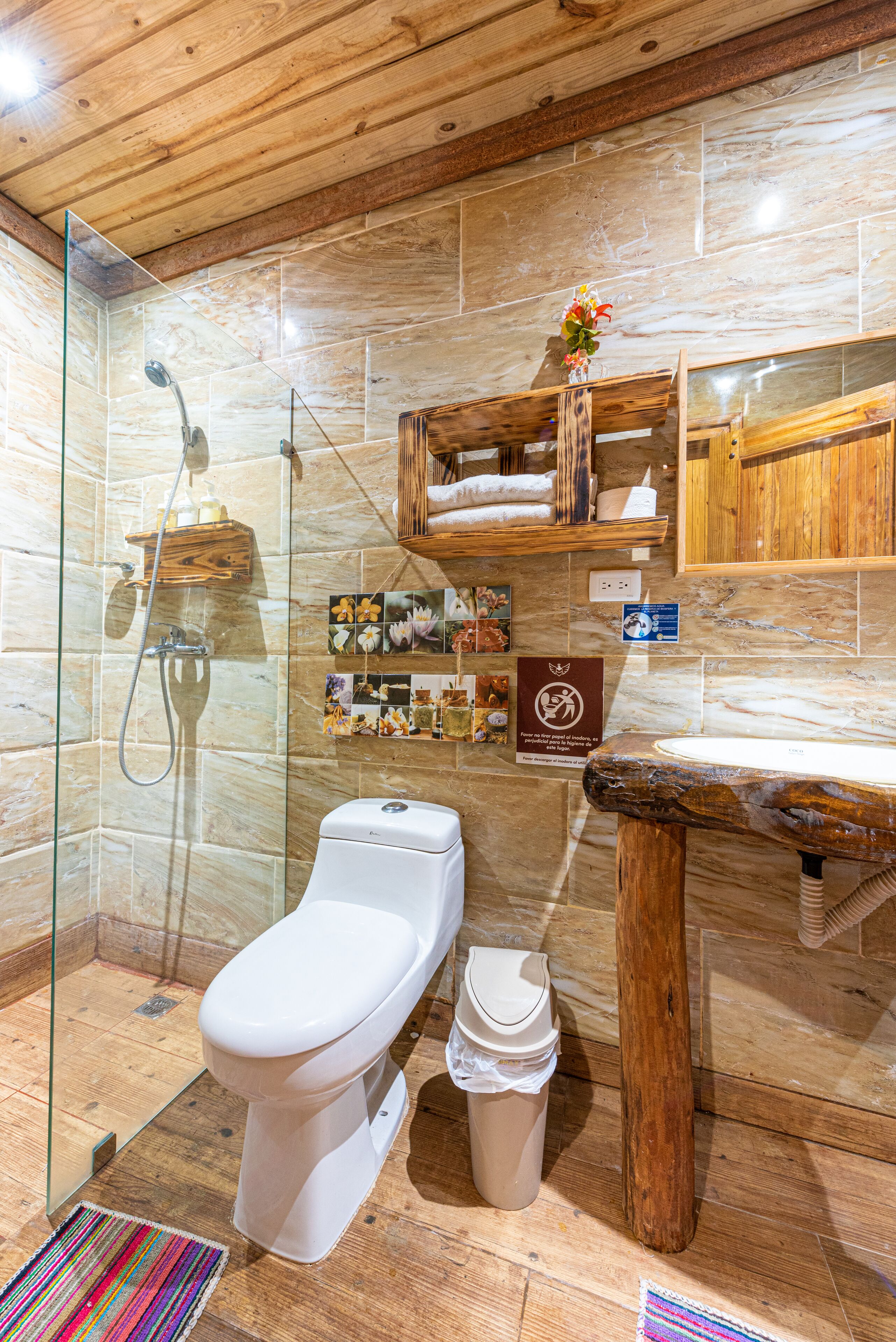 A modern bathroom with a glass-enclosed shower, a white toilet, a wooden vanity, and a marble-tiled wall.