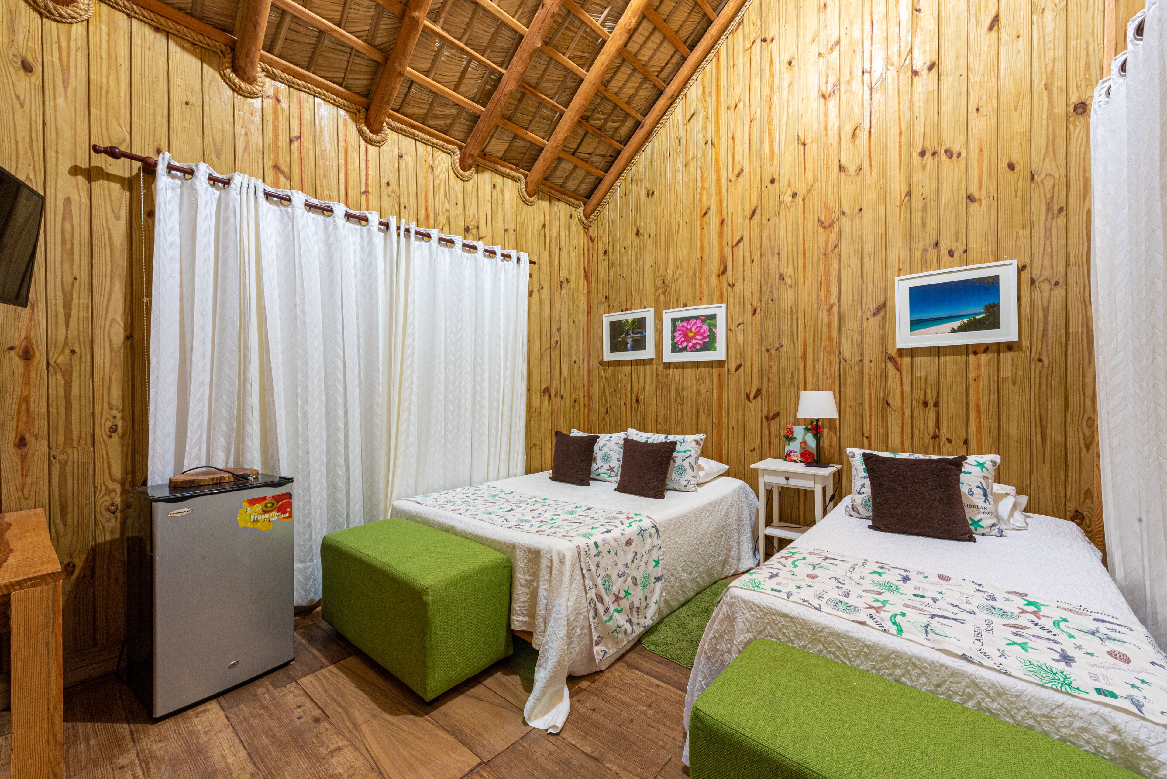A wooden cabin with two beds, a small refrigerator, and a green bench.